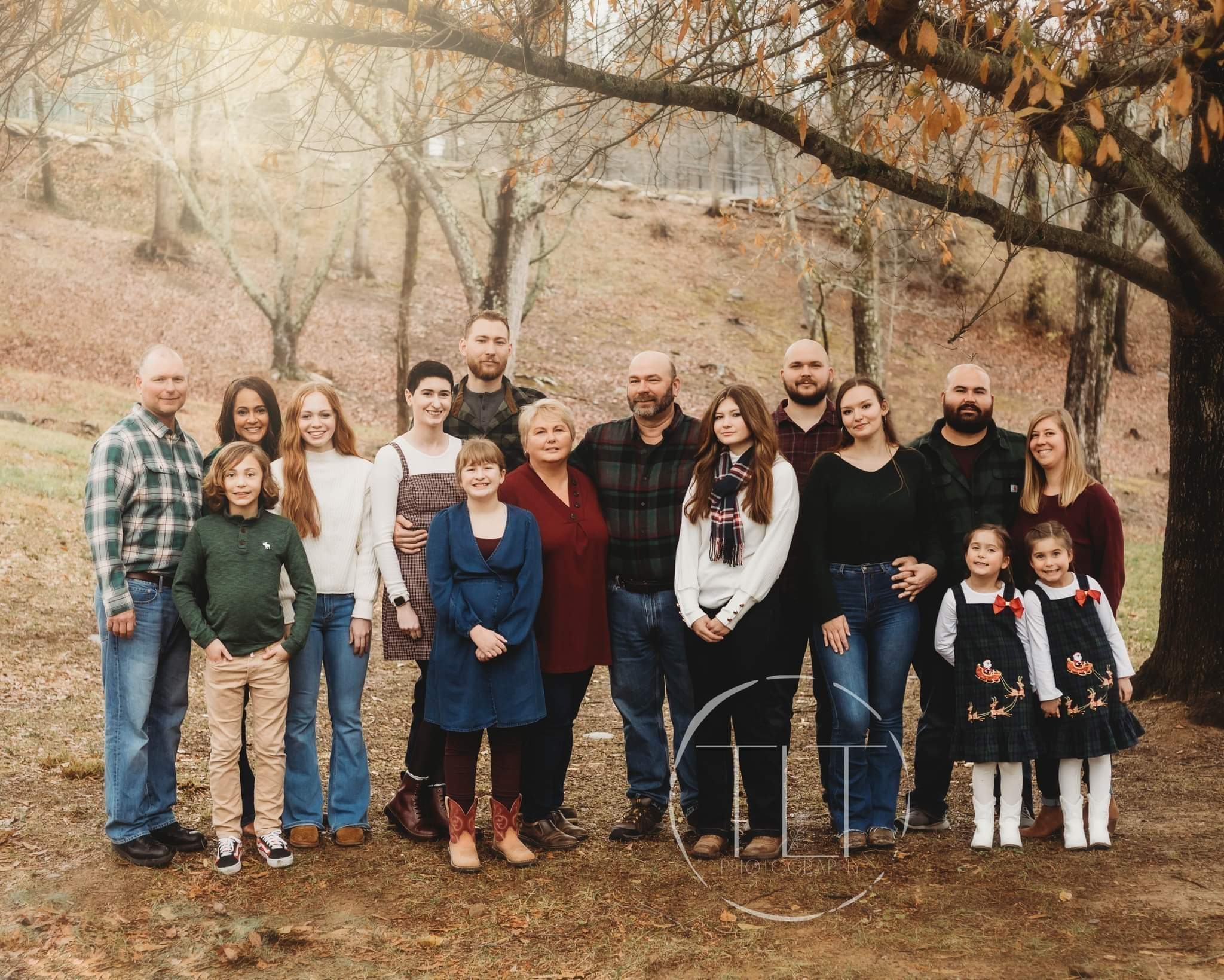 Large group of adults and children standing beneath autumn trees.